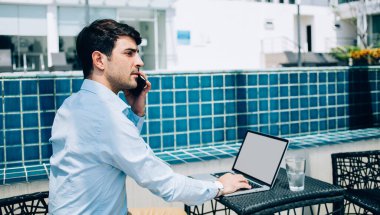 Mavi tişörtlü düşünceli etnik bir adamın bilgisayarında boş ekranla çalışırken akıllı telefondan güneşli terasta başka tarafa baktığı görüntüler.