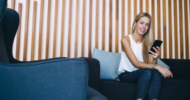 Neşeli beyaz kadın girişimci modaya uygun giyinmiş modern iç mekanlarda teknoloji kullanarak zaman geçiriyor, güzel kadın işyeri sahibi cep telefonundan mesajları kontrol ediyor.