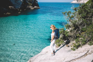 Sarışın bayanın günlük kıyafetleri ve güneş gözlükleriyle berrak mavi suyun üzerinde dikilirken başka tarafa baktığı ve yolculuğun keyfini çıkardığı