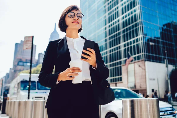 コンテンツの下からニューヨークの路上でスマートフォンや飲み物のテイクアウトコーヒーで正式な服や眼鏡メッセージングのエレガントなビジネス女性 — ストック写真