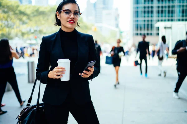 时尚的女商人穿着华丽的西装 头戴智能手机 喝着热饮 站在纽约繁华的大街上 看着镜头 — 图库照片