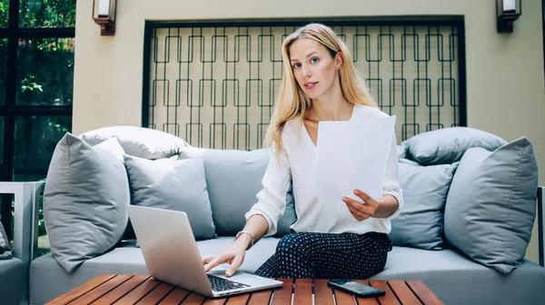 有决心的女企业家穿着雅致的服装 用上网本和工作时坐在沙发上 看着相机 — 图库照片