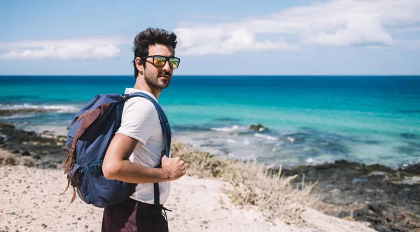 照片一半长 背景是带旅游背包的南亚男性 背景是海景 英俊的印度流浪者正在西班牙莫尔卡岛上游览风景如画的野生海滩 — 图库照片