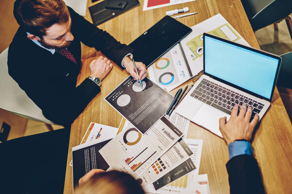 Experienced male marketers analyzing financial statistics during productive collaboration at table desktop with laptop computer with copy space area for business website, experts discussing trade