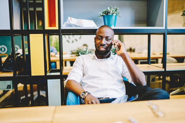 African American businessman talking with colleague using app on mobile phone during workflow in office interior, confident male owner of company making smartphone call for discuss project ideas