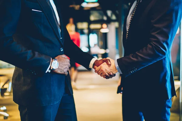 Cropped view of two multicultural entrepreneurs dressed in formal wear handshaking after successful deal during exchange meeting, business marketer greeting owner of company in modern office