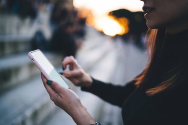 Günbatımına karşı modern binaların yakınında mesaj gösterirken, akıllı telefon kullanarak tanınmayan bir kadını tarla.