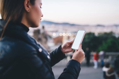 Şehirli meydanında akşamını geçirirken rahat giyimli, akıllı telefondan mesaj okuyan genç bir kadının yan görüntüsü