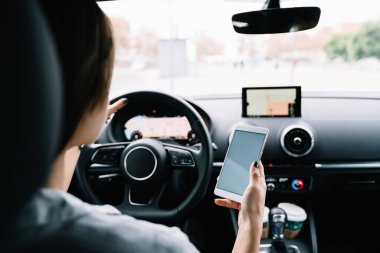 Çağdaş otomobilin sürücü koltuğundaki yüzü olmayan esmerin yol boyunca hoparlörle konuşurken cep telefonuyla konuşması.