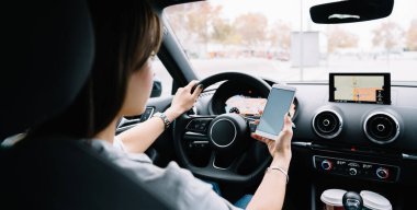 Güzergâh araması için akıllı telefon kullanan sıradan giysili genç bayanın araba sürerken ve ekrana bakarken arka plan görüntüsü