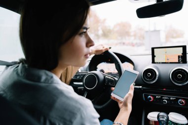 Arabada otururken ve başka tarafa bakarken akıllı telefonu yön bulma aracı olarak kullanan gündelik giysiler giymiş genç bir kadının arka plan görüntüsü
