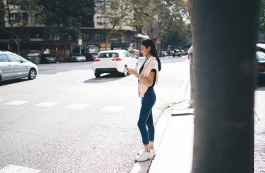 Gülümseyen Asyalı kadın yaya cep telefonuyla yolda duruyor. Şehirdeki navigasyon uygulamasını kullanıyor. Hücresel kontrol yapan bin yıllık bir kadın şehirde taksi durağını duyuyor.