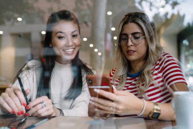 Gülümseyen beyaz kadın internet sayfalarına bakmak ve arkadaşlarıyla bilgi aramak için cep telefonu kullanıyor, akıllı telefona yeni uygulama yükleyen pozitif çok ırklı kızlar kafede 4G 'nin keyfini çıkarıyorlar.