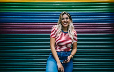 Gündelik kıyafetlerle gezen komik hippi kızın yarısı elinde dijital cihazlar ve arka planda fotokopi çekilecek yere yakın gülüyor. Akıllı telefon kullanan neşeli İspanyol vlogcu.