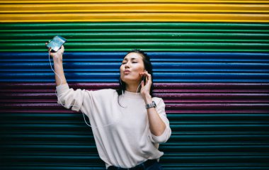 Dijital kulaklıklı, dertsiz, elektronik müzik eşliğinde internet medya reklamları için fotokopi alanı olan reklam duvarının yanında dans eden, cep telefonlu Asyalı hippi kız eğleniyor.