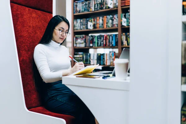 아시아 여성이 작성하고 타이핑 정보를 의자에 앉아서 작업하는 모습붉은 도서관에 — 스톡 사진