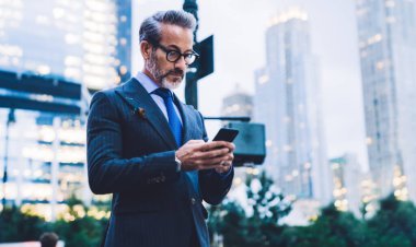 Yakışıklı, orta yaşlı, gözlüklü, takım elbiseli, telefonda yazan ve akşam vakti New York yolunda duran bir erkek.