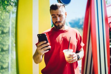 Kafası karışmış erkek blogcu çevrimiçi sohbet sırasında akıllı telefon mesajlarını kontrol etmek için içkiyle kafası karışmış, internetten rezervasyon ve bankacılık yapmak için mobil uygulama yükleyen Kafkasyalı adam