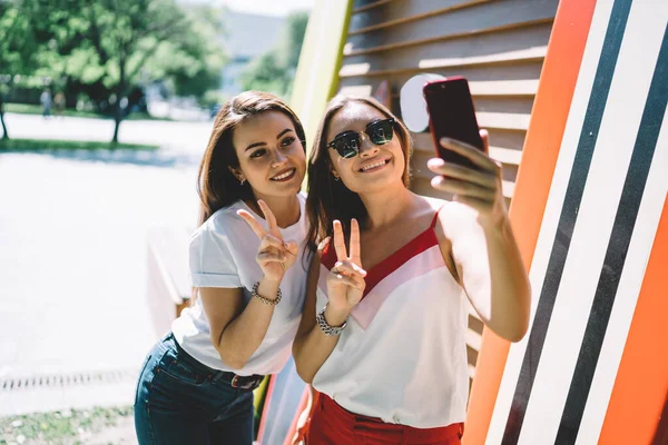 白人嬉皮士女孩一起制作自拍照片 利用智能手机前置摄像头分享自己的博客 快乐的女性朋友在拍摄影响视频时表现出V Sign — 图库照片