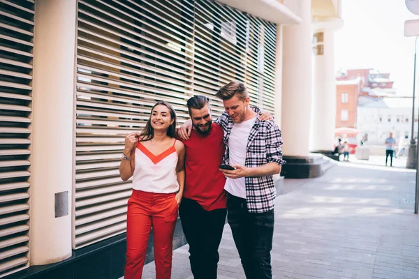 Group of young Caucasian men and woman walking at urban setting using cellphone gadget for tracking gps, happy male and female best friends in casual wear enjoying together pastime at city street