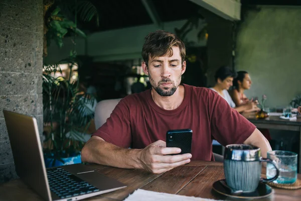 Ernstig Knappe Jonge Man Donkerrood Shirt Met Smartphone Aan Tafel — Stockfoto