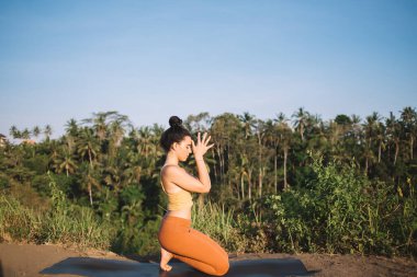 Düşünceli, konsantre olmuş, beyaz bir kadın, boş zamanlarında meditasyon yapıyor ve doğanın tadını çıkarıyor. Aktif giyinen genç bir kadın Asana 'da zihinsel ve fiziksel uyum üzerine yoğunlaşıyor.