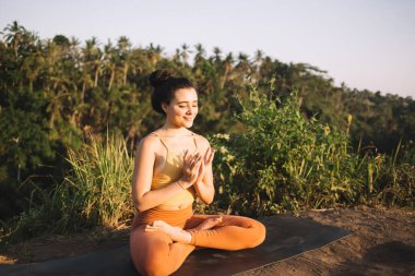 Aktif haldeki neşeli beyaz kadın sahada oturmuş ruhani meditasyonla uyum içinde yaşıyor, 20 'li yaşlarda aktif giyinmiş, Lotus poziyonunda dinleniyor zihinsel sağlığını ve sağlığını koruyor.