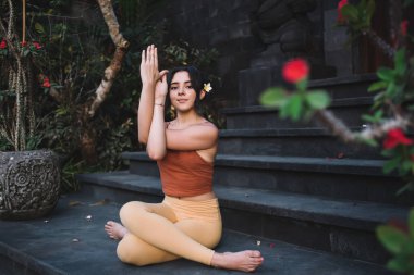 Aktif haldeki sakin bir kadının portresi. Bedenini hissetmek ve fiziksel sağlık için kaslarını germek. Düşünceli bir kadın, dışarıda, tapınağın yanında manevi sağlık için oturarak yoganın tadını çıkarıyor.