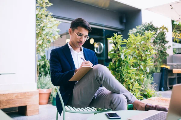 Başarılı modaya uygun giyinmiş modaya uygun erkek yazar dizüstü bilgisayarla terasta yazı hazırlıyor, kendine güvenen işadamı teknoloji üzerinde çalışırken planlarını kontrol ediyor.
