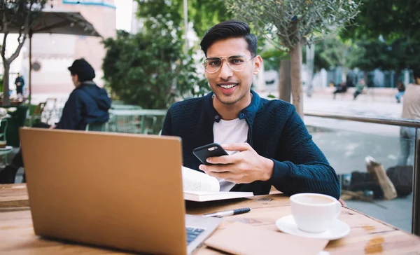 Sorrindo Jovem Étnico Desgaste Casual Óculos Usando Smartphone Enquanto Trabalhava — Fotografia de Stock