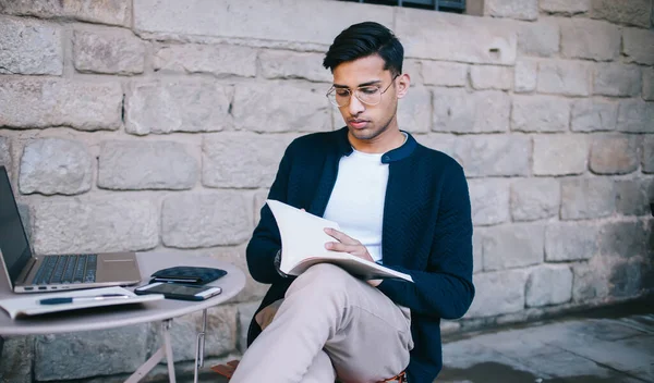 Modern kafeteryada bilgisayarla uğraşırken gözlük takan ve günlük giysiler giyen konsantre etik bir serbest meslek sahibi.