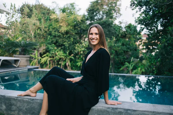 Joven Mujer Alegre Vestido Largo Negro Sentado Borde Piscina Mirando — Foto de Stock