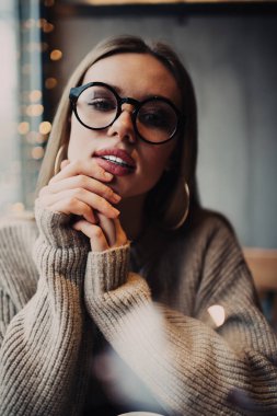 Göz düzeltmesi için optik gözlüklü modaya uygun hippi kızın yarım boy portresi boş zamanlarında kameraya bakıyor güzel beyaz kadın 20 'li yaşlarda şık gözlüklü poz veriyor.