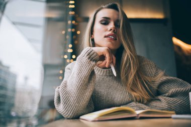 Çalışmak ve sınava hazırlanmak için zaman harcayan zeki kız öğrencinin portresi eğitim notlarıyla kafe masasında oturuyor, ders kitabıyla yetenekli bir şair kameraya bakarken bir yandan da metin yazıyor.