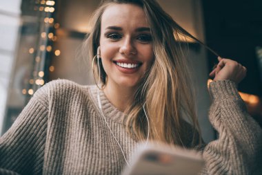 Elektronik kulaklıkla neşeli beyaz kuşak Y 'nin yarım boy portresi boş zamanlarında pozitif ses yayını dinliyor modern kulaklıklarda kameraya gülümseyen neşeli kadın milenyumu.