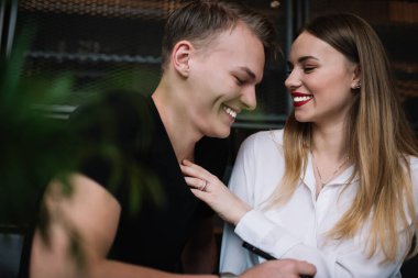Gözleri kapalı neşeli genç bir çift, birlikte vakit geçirirken gülüyorlar. Beyaz bluzlu sevgili, sevgilinin boynuna hafifçe dokunuyor.