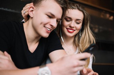 Kafe 'de masada oturup akıllı telefondan internette sörf yapan ve modern kafede birlikte vakit geçiren neşeli genç bir çift.