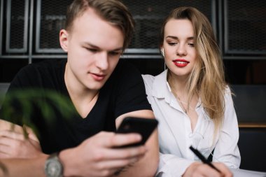 Hafta sonu modaya uygun kız arkadaşıyla kafede dinlenirken cep telefonu kullanan şık yakışıklı adam ekrana bakıyor ve notlar yazıyor.