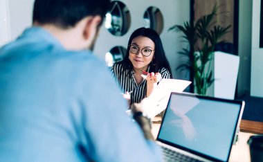 Genç Asyalı bayan müşteri dizüstü bilgisayarla ürün yöneticisinin önünde oturuyor ve proje tartışılırken belge hakkında sorular soruyor