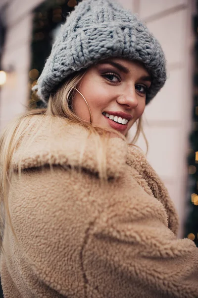 Half length portrait of prosperous Caucasian woman with perfect white veneers smiling at camera during winter photo session, cheerful female model 20 years old in trendy outfit posing outdoors