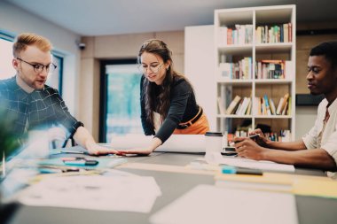 Genç hevesli meslektaşlardan oluşan çok ırklı bir ekip birlikte strateji üzerinde çalışıyor ve hafif modern ofiste seçenekleri ve fikirleri tartışırken gülümsüyor.