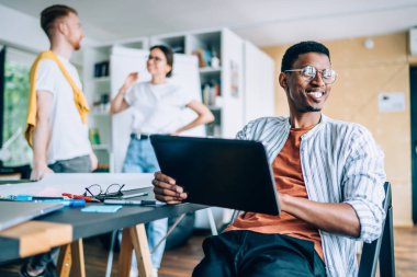 Tabletle oturmuş gülümseyen siyah bir adam ve etkin erkek ve kadın arkadaşları kütüphanede sohbet ederken gözlerini kaçırıyor.
