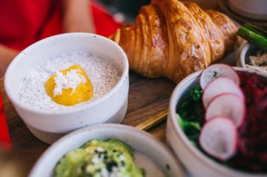 Sabah kahvaltısı için taze chia yoğurdu ve mango püresi ile masada oturan kadın kafeterya ziyaretçisinin görüntüsü. Ev yapımı sağlıklı meyveler ve pişirilmiş kruvasan ile lezzetli tatlı bir brunch yemeği.