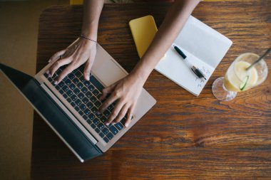 Çevrimiçi planlama yapmak için modern dizüstü bilgisayar kullanan yetenekli kadın serbest yazar, kafeteryada smoothie kokteyli ve eğitim not defteriyle oturuyor, klavye üzerine web yazısı yazan kadın