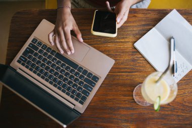 Bistro ziyareti sırasında medya dosyalarını paylaşmak için cep telefonu aygıtı ve dizüstü bilgisayar kullanan yetenekli bir kadın, cep telefonu sohbeti sırasında eğitim kitabı yazan eğitimli serbest bir kadın.