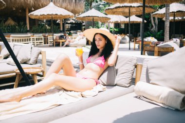 Havalı şapkalı ve bikinili güzel beyaz kadın güneşli yatakta uzanmış, dinlenirken dinleniyor, tatilde sıska ve seksi vücudunu bronzlaştıran çekici hippi kız.