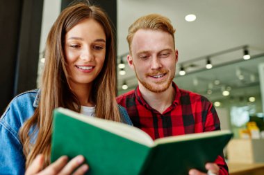 Eş öğrenim sırasında analiz için eğitim bilgisi okuyan zeki erkek ve kadın öğrenciler, bilgi defterinden notları kontrol eden Kafkas hippiler proje oluşturulmasını tartışıyorlar.