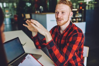 Mutlu kızıl saçlı adam, birlikte çalışma alanından kazanç sağlamayı planlayan, kırpılmış kadın ve beyaz iş arkadaşlarıyla yaptığı dostça beyin fırtınası toplantısında bilgi açıklıyor.