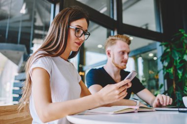 Görme düzeltmesi için klasik gözlüklü beyaz kız öğrenci güncelleme uygulaması için hareketlilik bildirimini kontrol ediyor, çevrimiçi akıllı telefon sohbeti sırasında çekici milenyum mesajı gönderiyor
