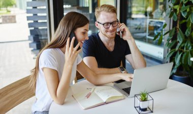 Başarılı hipster öğrencileri müşteri hizmetlerini aramak ve kablosuz bağlantıyı tartışmak için akıllı telefon cihazları kullanıyor, cep telefonuyla konuşan mutlu erkek ve kadın cep telefonları ile bilgisayardan webinar izliyorlar.